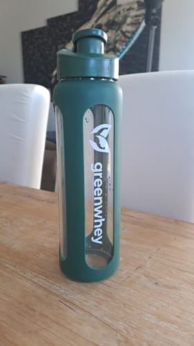Photo d'un client montrant le GreenShaker 2.0, en verre avec une protection verte, posé sur une table.