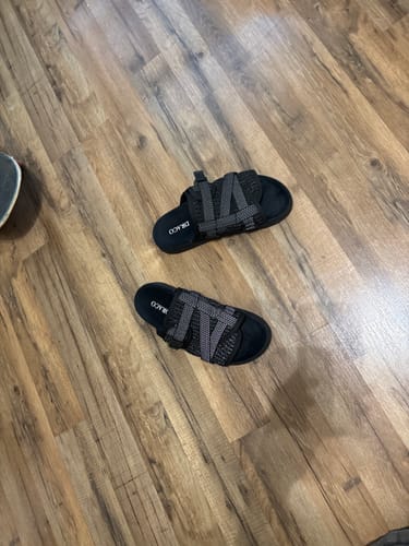 Customer's pair of black Reflective Dracoslides with woven straps, shown on a light brown wood floor.