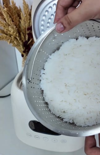 Reviewer lifting the perforated basket of cooked rice from the white Eurohauz Healthy Rice Cooker.