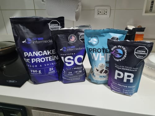 Cliente muestra el envase de PR - Mezcla Energizante junto a otros suplementos en una encimera de cocina.