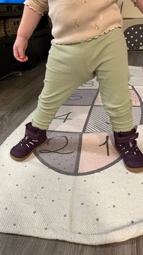 Asiakkaan lapsen jalassa uudet kirsikanpunaiset Vaistoa Kaste -paljasjalkakengät.