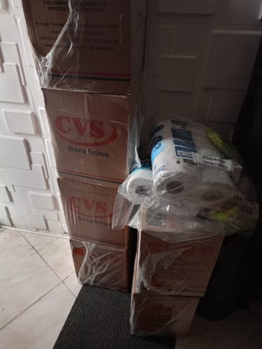 Cliente mostrando as caixas empilhadas do kit Cesta Básica Econômica que recebeu.