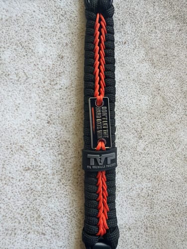 Close-up of a customer's black and orange paracord bracelet with its "Don't Let The Hard Days Win" tag.