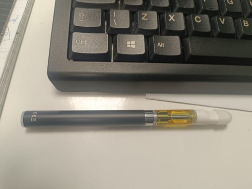 Customer's 10-OH HHC Superior Live Resin Cartridge attached to a dark vape pen, resting on a white desk by a keyboard.
