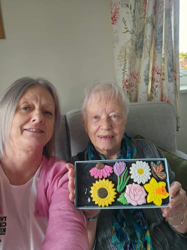 Customer and a companion holding the open Flowers Deluxe Biscuit Box, showing the colorful flower biscuits inside.