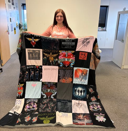 Customer holding a large Project Repat T-Shirt Quilt made from various Bon Jovi concert t-shirts in a room.
