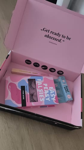 Rezensent zeigt den geöffneten, rosa Versandkarton mit dem Produkt 'seal the deal. TOP COAT CLEAR' und Wimpern.