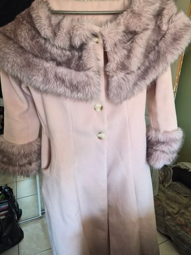 Le manteau crème de la cliente suspendu, avec un large col et des poignets en fourrure foncée.