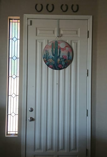 Reviewer's round Cactus Door Hanger hanging on a white front door with a stained glass window.