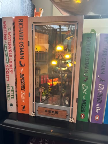 Customer's assembled Kyoto Gion Book Nook Kit glowing with warm light on a bookshelf between other books.