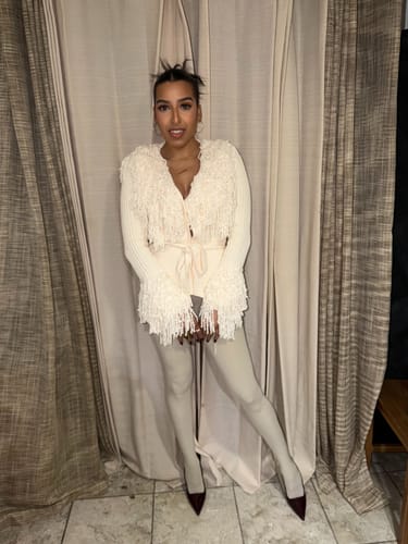 Reviewer poses indoors wearing the light-colored Naked Closed Toe Legging with a fringe cardigan and heels.