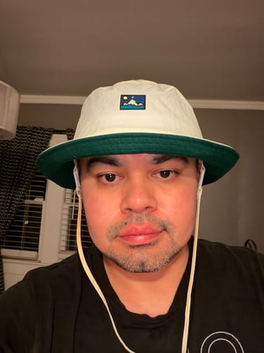 Close-up of a reviewer wearing the cream Big Wicking Bucket Hat with a green brim.