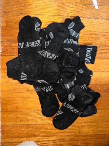 Reviewer's pile of black Men's Alpaca Socks with grey patterns on a wooden floor.