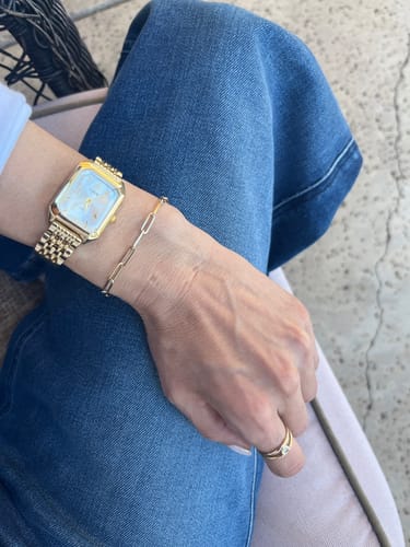 Reviewer's wrist showing the gold CLAIRE DE MAINS watch with a light face, styled with a delicate gold bracelet and ring.