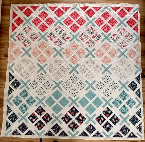 Customer's finished Skylight Quilt Kit top laid on a floor, showing its colorful geometric pattern.