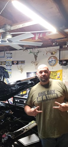 Customer wearing the olive green 'One Day At A Time' t-shirt in a garage.