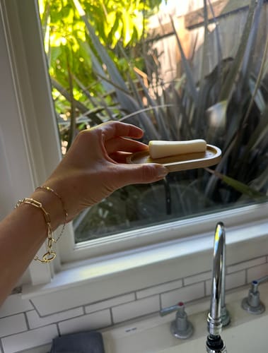 Reviewer holding the Vegan Stain Remover Bar on a wooden dish by a sink.