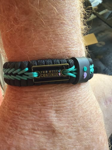 Customer's wrist showing the black and teal paracord bracelet with its 'You Must Continue;' plate and semicolon symbol.