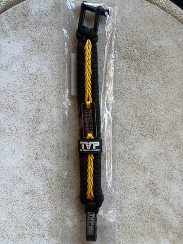 Customer's black and yellow Keep Moving Forward paracord bracelet shown in its original clear packaging on a table.