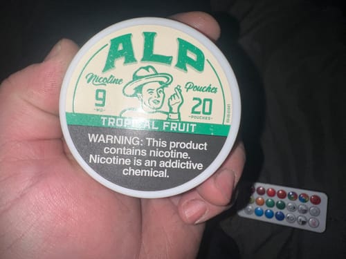 Customer holding a round can of ALP Tropical Fruit Nicotine Pouches in their hand.