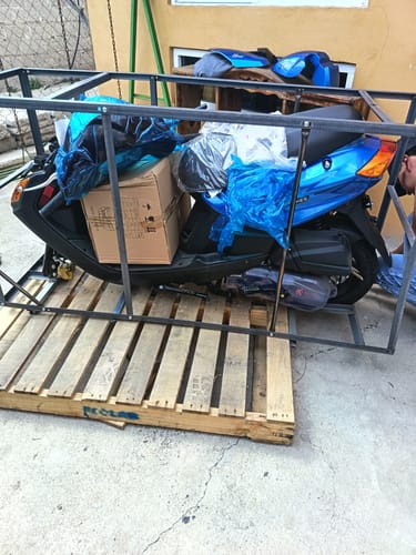 Cliente muestra su nueva motocicleta Acapulco Kiwo 150 azul dentro de la jaula metálica de envío.