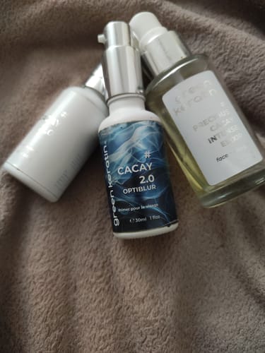 Photo d'un client du primer CACAY 2.0 OPTIBLUR parmi un trio de produits de soin sur une surface douce.