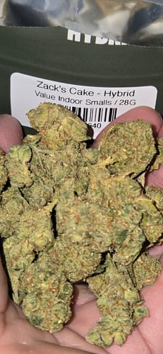 Customer holding a handful of green Value Indoor Smalls buds in front of the product's packaging.