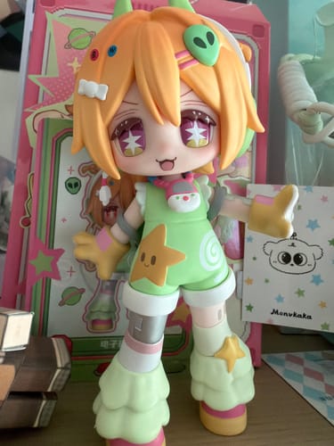 Customer's cute TOMIZ Electronic Pet figure, an alien-themed doll with orange hair and a green and yellow outfit, standing on a desk.