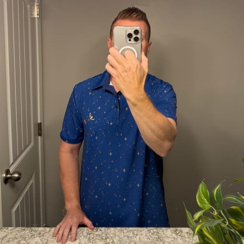 Reviewer taking a mirror selfie wearing the blue, star-patterned Peter Pan "Second Star to the Right" polo shirt.