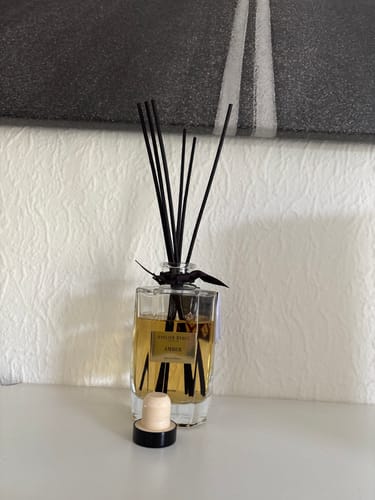 Klant's Amber Geurstokjes in de glazen fles met zwarte stokjes, opgesteld op een plank.