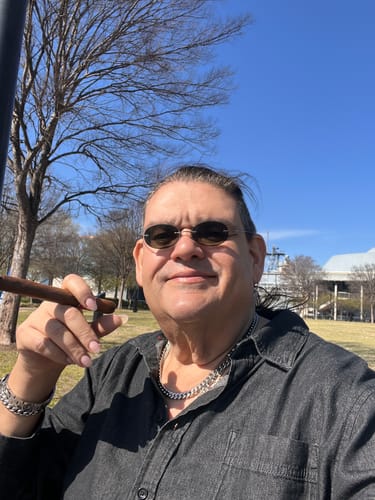 Reviewer holding a Cherry Dosi-Do Pre-Roll while sitting outside in a park on a sunny day.