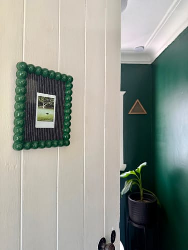 Reviewer's dark green Windsor Button Frame hanging on a white door, matching the wall color of the room behind.