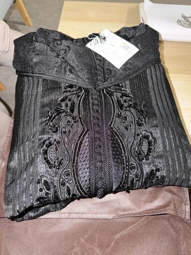 Customer's folded black Jellaba Rina, showing the intricate embroidery and pleated fabric on a table.