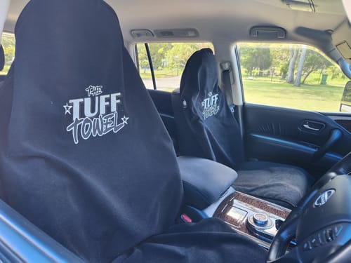 Reviewer's two black Waterproof Car Towel Seat Covers fitted over the front leather seats of a car.
