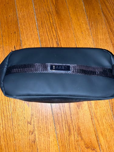 Customer's black Toiletry Bag with a logo strap, shown on a wooden surface.