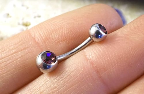 Close-up of a reviewer holding the small, silver Petite Ball Classique Belly Bar with dark purple gems.