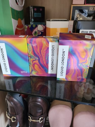 Reviewer shows three boxes of the For Her Pheromone Perfume in colorful packaging on a shelf.