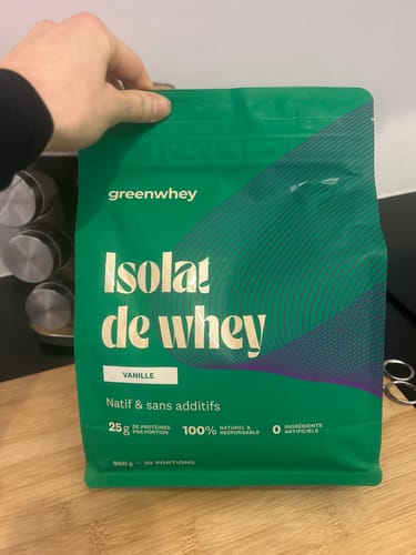 Client tenant le sachet vert d'Isolat de Whey Native saveur vanille dans une cuisine.