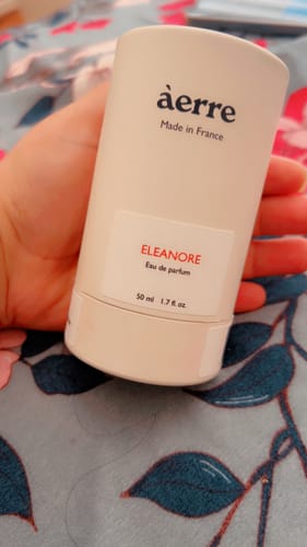 A customer's hand holds the white, cylindrical bottle of Eleanore eau de parfum.