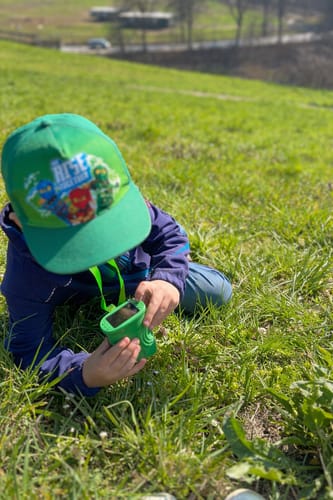 Rezensent zeigt ein Kind, das mit dem grünen Abenteuer-Mikroskop im Gras forscht.