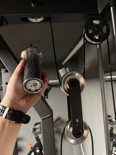 Kunde hält den silbernen Weight Stack Pin an das Seilzugsystem einer Kraftstation.