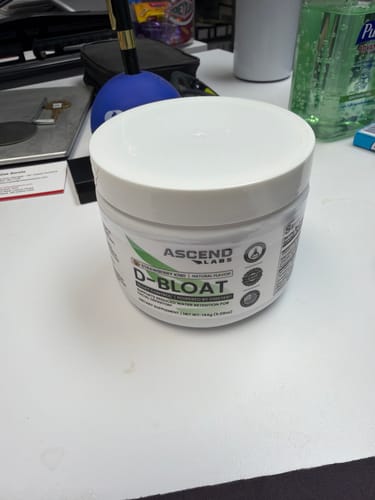 Customer's white container of D-BLOAT powder sitting on a desk.