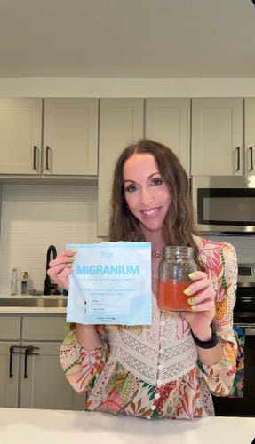 Reviewer holding a pouch of Migranium Daily and a glass of the mixed drink in her kitchen.