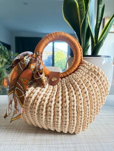 Reviewer's finished Shell crochet Handbag in beige, with a wrapped circular handle and a patterned scarf tied to it.