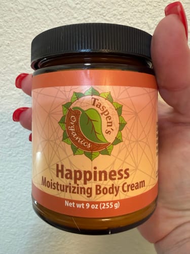 Customer's hand holding a 9 oz jar of Happiness Moisturizing Body Cream.