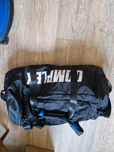 Customer's black Complex Duffle Bag with large white branding, seen from above on a wood floor.