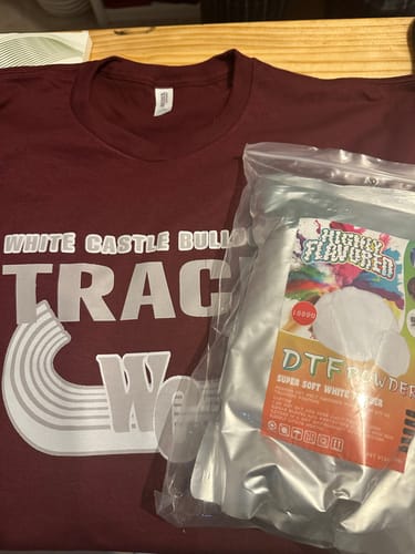 Customer's bag of DTF Super Soft Powder next to a maroon t-shirt with a large, white graphic print.