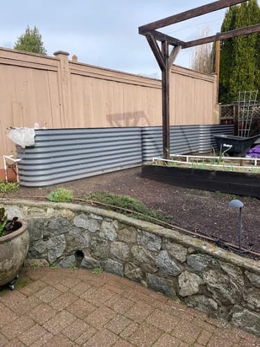 Customer's long, gray modular garden bed assembled along a fence in a backyard, ready to be filled.