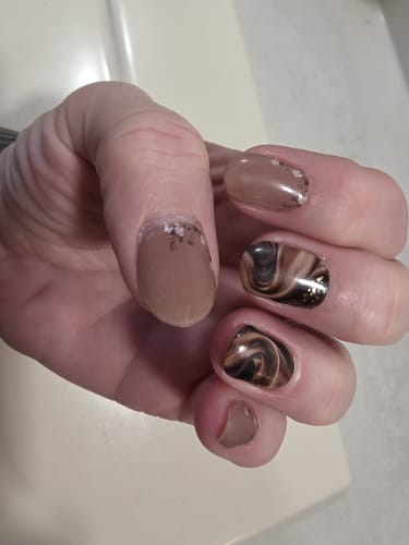 Rezensentin zeigt ihre Hand mit einer Maniküre. Die Nägel haben ein braunes Marmor- und Glitzer-Design.