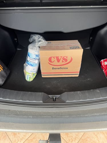Caixa da Cesta Básica Econômica Kit do cliente com um pacote de papel higiênico no porta-malas de um carro.